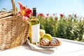 Composition with picnic basket and bottle of wine on wooden table in lily field. Space for text Royalty Free Stock Photo