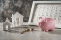 Composition with piggy bank, calendar and model of house and family on grey table. Concept of saving money for buying new house Royalty Free Stock Photo