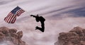 Composition of silhouetted figure jumping holding american flag against mountains and cloudy sky