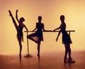 Composition from silhouettes of three young dancers in ballet poses on a orange background. Royalty Free Stock Photo