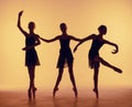 Composition from silhouettes of three young dancers in ballet poses on a orange background.