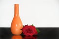Composition of single red rose beside of orange vase on black table Royalty Free Stock Photo