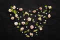 Composition of small pink roses and small green leaves on a black background forms a heart Royalty Free Stock Photo