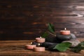 Composition of spa stones, green leaves and burning candles on wooden table Royalty Free Stock Photo