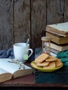 The composition of a stack of old books, open book, tea cups, glasses and plates of sugar cookies on a wooden background. Vintage. Royalty Free Stock Photo