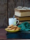 The composition of a stack of old books, tea cups, glasses and plates of sugar cookies on a wooden background. Vintage photo. Side Royalty Free Stock Photo