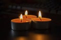 Composition of three candles on dark luxury night background. Black table, side view. Candles Burning at Night. Orange taper