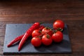 Composition of tomato bunch and hot pepper on black piece of board, top view, close-up. Royalty Free Stock Photo