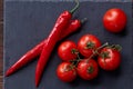 Composition of tomato bunch and hot pepper on black piece of board, top view, close-up. Royalty Free Stock Photo