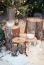 The composition of two decorative candles in glass on a snow-covered tree stump in the woods. Royalty Free Stock Photo