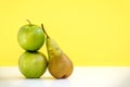 The composition of two fresh green apples and one long pear on yellow background Royalty Free Stock Photo