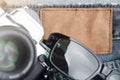 composition of vintage SLR camera and sunglasses on worn jeans around blank leather plate - travel and blogger concept - close up Royalty Free Stock Photo