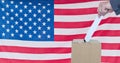 Composition of woman casting vote into ballot box against american flag Royalty Free Stock Photo