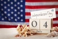 Composition with wooden calendar and card on sand against USA flag. Happy Independence Day