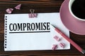 COMPROMISE - word on a white sheet on a wooden brown background with a cup of coffee and a pen