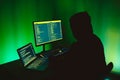 Computer hacker silhouette of hooded man typing on computer in a dark green room. Royalty Free Stock Photo