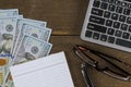 Computer keyboard with dollar money on notepad, pen and glasses wooden table