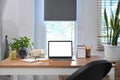 Laptop, alarm clock, potted plant and coffee cup on wooden table.