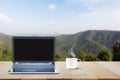 Computer laptop with black screen and hot coffee cup on wooden table top on blurred mountain background Royalty Free Stock Photo