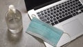 Computer laptop with medical face mask, notepad and pen on top of it together with a cup of coffee on dining table. Home Royalty Free Stock Photo