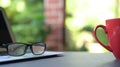 Computer laptop with reading glasses and coffee in red cup with garden background. Work from home Royalty Free Stock Photo