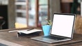 Computer laptop with white screen, coffee cup and notebook on working table in front of blur living room. Royalty Free Stock Photo