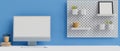 Computer with mock-up screen on white table with stationery and decoration on shelf on blue wall, 3D rendering