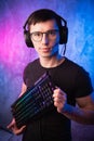 Computer nerd with keyboard over colorful pink and blue neon lit wall