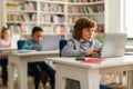 Computer science class. School boy sitting at desk at classroom with classmates on background, typing on laptops Royalty Free Stock Photo