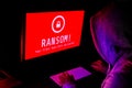 Computer Screen With Ransomware Attack Alerts In Red And A Hacker Man Keying On Keyboard In A Dark Room, Ideal For Online