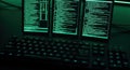 Computer screens displaying lines of green code in a dark room with a keyboard in the foreground Royalty Free Stock Photo