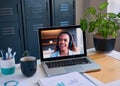 A computer shows a woman on a conference call, with hybrid work office and home