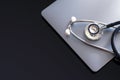 Stethoscope and laptop computer isolated on dark background.