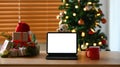 Tablet, coffee cup and gift boxes on wooden table near Christmas tree at home. Royalty Free Stock Photo