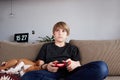 Concentraited young boy playing video game console seated on a sofa with basenji dog puppy sleeping close in living room Royalty Free Stock Photo