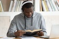 Concentrated african american guy reading book in earphones.