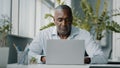 Concentrated african man employee american expert focused specialist sits in office works on laptop use personal Royalty Free Stock Photo