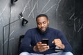 Concentrated african man sitting on couch looking at cell screen