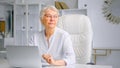 Concentrated aged lady manager in glasses sitting on large chair at table