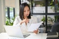 Concentrated Asian businesswoman reviewing or examining business reports at her desk