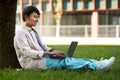 Concentrated asian man sitting under tree, working on his laptop Royalty Free Stock Photo