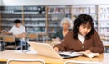 Concentrated asian teenager female schoolgirl sitting at library desk, doing homework with internet Royalty Free Stock Photo