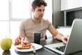 Concentrated attractive man using laptop while eating breakfast Royalty Free Stock Photo