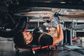 Concentrated auto mechanic male working alone on the floor repairing bottom of the car, look at details, troubleshoot the car