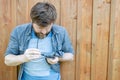 Concentrated man carefully cleans glasses from dust, wiping them with a shirt, against a background of a wooden wall