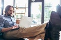 concentrated bearded man using laptop and drinking coffee from