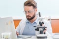 Concentrated bearded scientist working with microscope and laptop