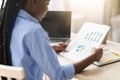 Concentrated black businesswoman checking financial reports, economic graphs and charts at workplace