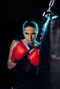 Concentrated boxer in red boxing gloves looking at punching bag on black.