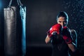 Concentrated boxer in red boxing gloves standing under water drops on black.